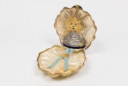 View of open gold shell case showing white satin lining, perfume bottle fitted into top half an…