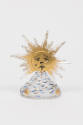 Glass perfume bottle in the shape of a bumpy mountain with blue accents and a gold sunburst on …
