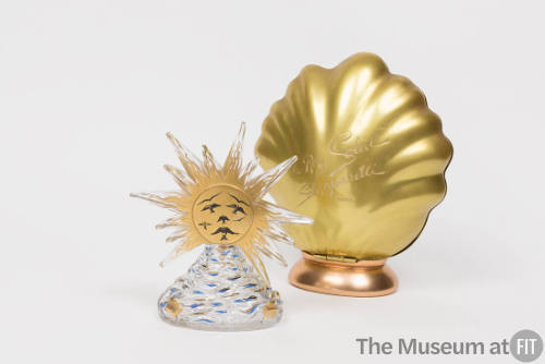 Glass perfume bottle in the shape of a gold sunburst rising over a mountain with a gold shell s…