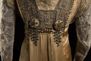 Detail view of copper dress bodice showing bottom of beaded panel and two embroidered medallion…