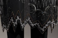 Detail view of black evening jacket showing bottom scalloped hem outlined with pearls and silve…
