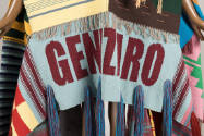 Detail view of wrap coat showing light blue panel with dark red “Genizario” text and large tuft…
