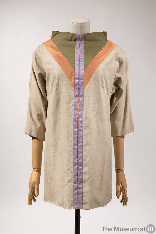 Beige ¾ sleeve tunic top with funnel neck trimmed with a green triangle outlined in orange and …