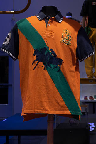 Man’s orange polo shirt with navy blue short sleeves and collar, a diagonal green stripe and la…