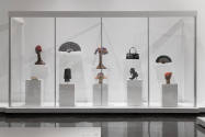 Art X Fashion exhibition installation view of ten shoes, bags, fans and hats on white pedestals…