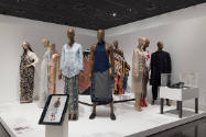 Art X Fashion exhibition installation view of many dressed mannequins, a tablet and shoes in a …