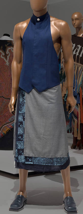 Ensemble of blue waistcoat vest with single button at neck, grey and blue batik layered wrap sk…