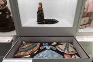 Doll Dressing exhibition installation view of a case containing an 1860s doll with coordinating…