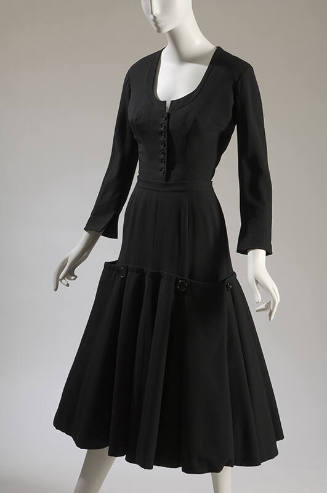 Black two-piece dress with scoop neck, long sleeves, and calf-length skirt with button on flare…