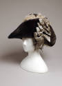 Blue velvet hat with four silver bows on right side and grey feathers in plume