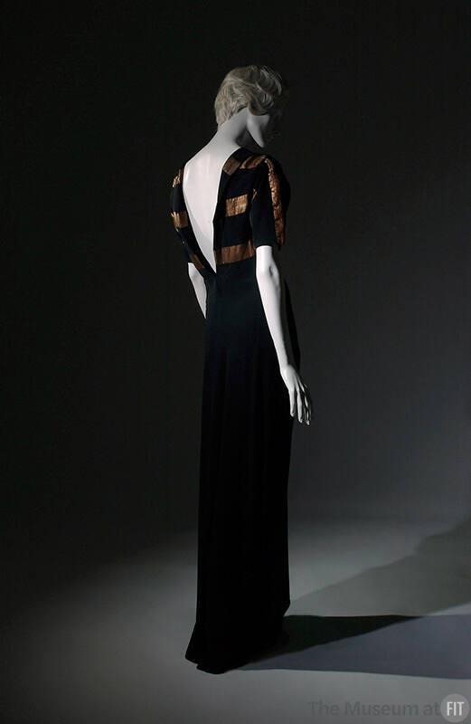 Back view of black floor-length evening dress with deep V-back and thick bronze stripes across …
