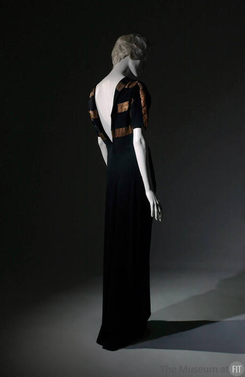Back view of black floor-length evening dress with deep V-back and thick bronze stripes across …