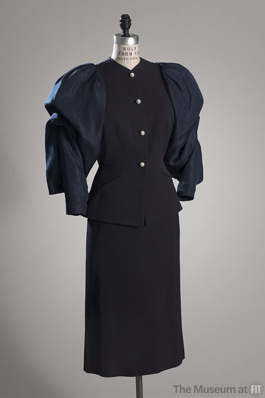 Navy cocktail suit of jacket with voluminous sleeves and pearl buttons and calf-length straight…