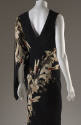 Back view of black sleevless evening dress with spiraling beige lily print, cape effect over le…