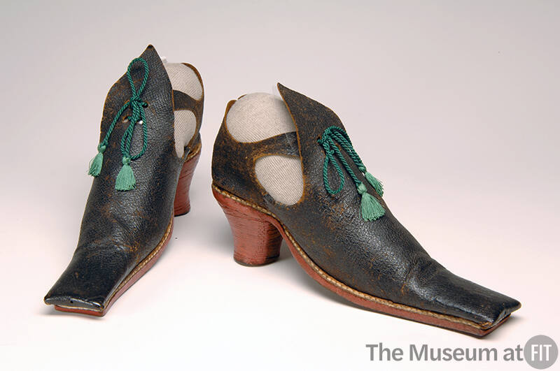 Front & 3/4 view of long square toed black leather shoes; red heels, open sides; green tassel t…