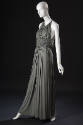 ¾ view of grey halter neck floor length evening gown with midriff smocking panel creating gathe…