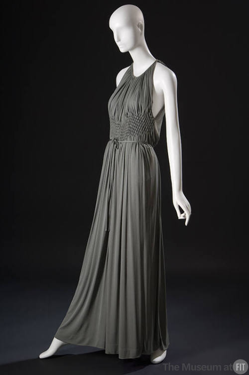 ¾ view of grey halter neck floor length evening gown with midriff smocking panel creating gathe…