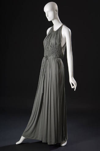 ¾ view of grey halter neck floor length evening gown with midriff smocking panel creating gathe…