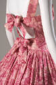 Back view of pink and white rose print cocktail dress showing cut out in low back with bow ties…