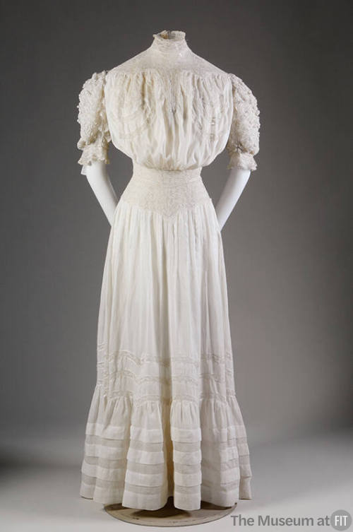 White floor length cotton lawn dress with stand collar, elbow length puffed sleeves, fitted wai…