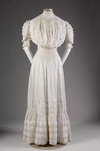 White floor length cotton lawn dress with stand collar, elbow length puffed sleeves, fitted wai…