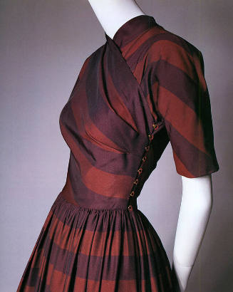 Detail view of red and purple striped dress showing bias cut bodice with high neck and brass ho…