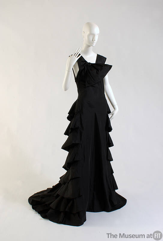 Sleeveless floor length black evening tress, draped bow at right shoulder, tiered flounce skirt