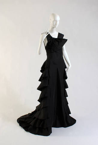 Sleeveless floor length black evening tress, draped bow at right shoulder, tiered flounce skirt