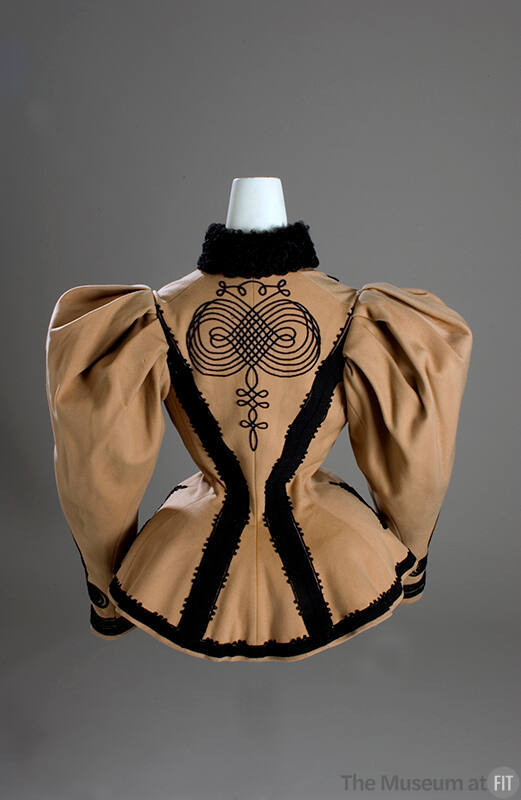 Back view of tan skating jacket with black Persian lamb collar, black braid and trim throughout…