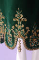 Detail view of green velvet dress embroidery at scalloped hem showing gold metallic floral moti…