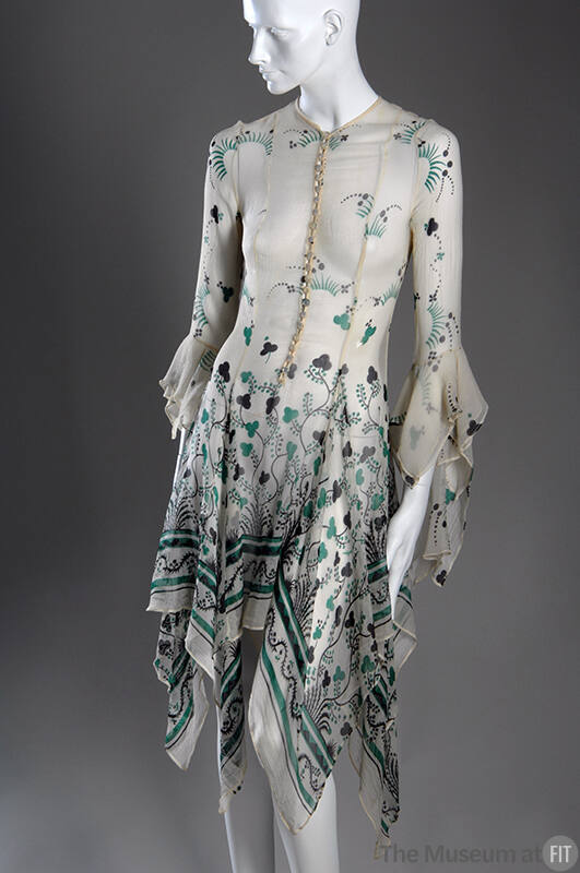 Off-white sheer button front dress with green and black shamrock print, handkerchief hem