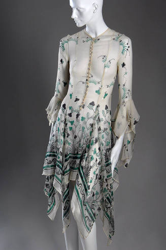 Off-white sheer button front dress with green and black shamrock print, handkerchief hem