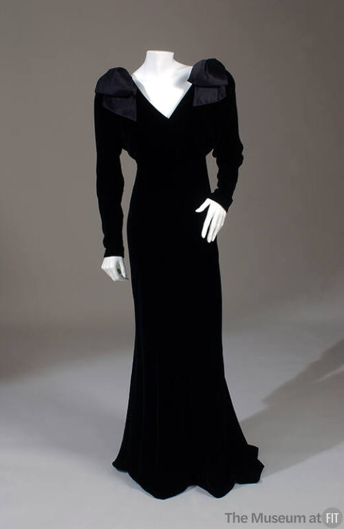 Black velvet floor length V-neck gown with long dolman sleeves and large shoulder bows