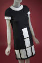 Detail of black mini dress with white vinyl collar, short sleeves and white rectangles at front…