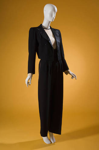 Black tuxedo with short jacket with satin lapels, off-white pleated top, black pants and cummer…