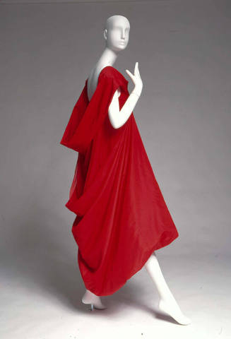 Red evening dress with high front neckline that is doubled, folded and bias cut at the back to …