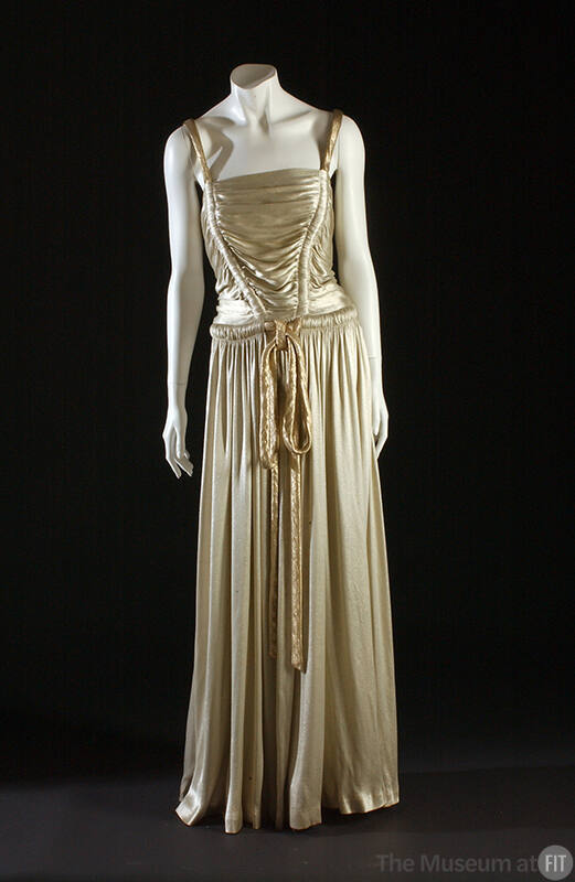 Ivory lamé floor length gown with gold lamé rouleau shoulder straps and tie belt and shirred bo…