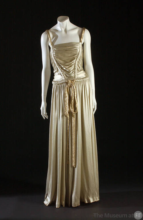 Ivory lamé floor length gown with gold lamé rouleau shoulder straps and tie belt and shirred bo…