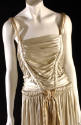 Detail view of gold lamé gown shoulder straps encased in shirred bodice and extended around wai…