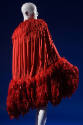 Red evening cape smocked along curved edges of cocoon silhouette, crimson feather trim forming …