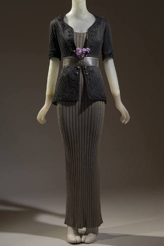 Black elbow length floral brocade jacket over floor length grey ribbed sweater dress and purple…