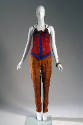 Red corset made of red, blue and brown beads with brown bra top underneath and copper pants wit…