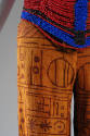 Detail view of red, blue and brown beaded corset and brown geometric designs on copper pants