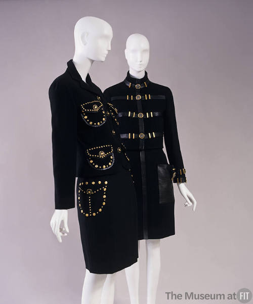 Two black suits: left with gold studs outlining large flap pockets and right with leather bands…