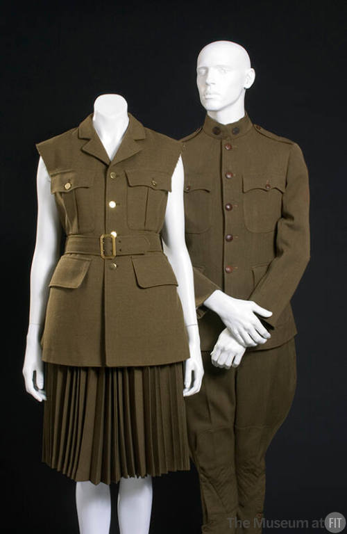 Women’s green sleeveless jacket with matching pleated, knee length skirt shown with a man’s gre…