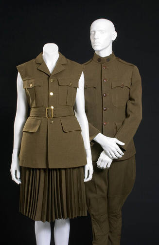 Women’s green sleeveless jacket with matching pleated, knee length skirt shown with a man’s gre…