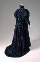 Back view of long-sleeved black evening dress with apple motifs, scalloped collar, and long fla…