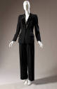 Black tuxedo pantsuit with double princess seam angled at waist, padded shoulders; wide straigh…