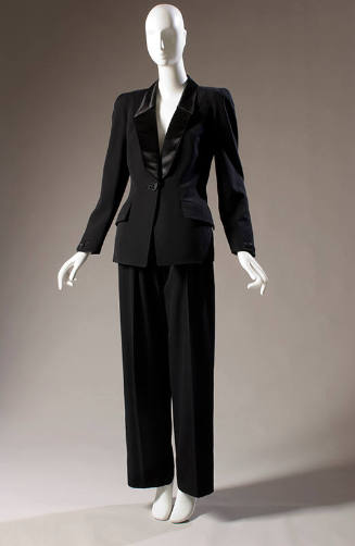 Black tuxedo pantsuit with double princess seam angled at waist, padded shoulders; wide straigh…