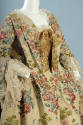 Detail of floral pattern brocaded silk gown bodice with lace trimmed neckline with gold bow and…